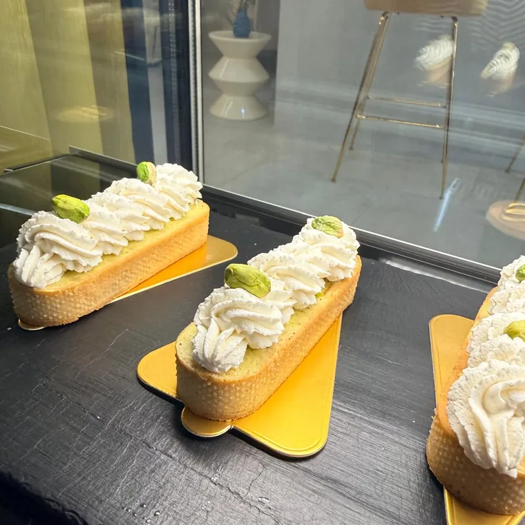 Éclairs de pasta choux con crema montada y pistacho sobre base dorada